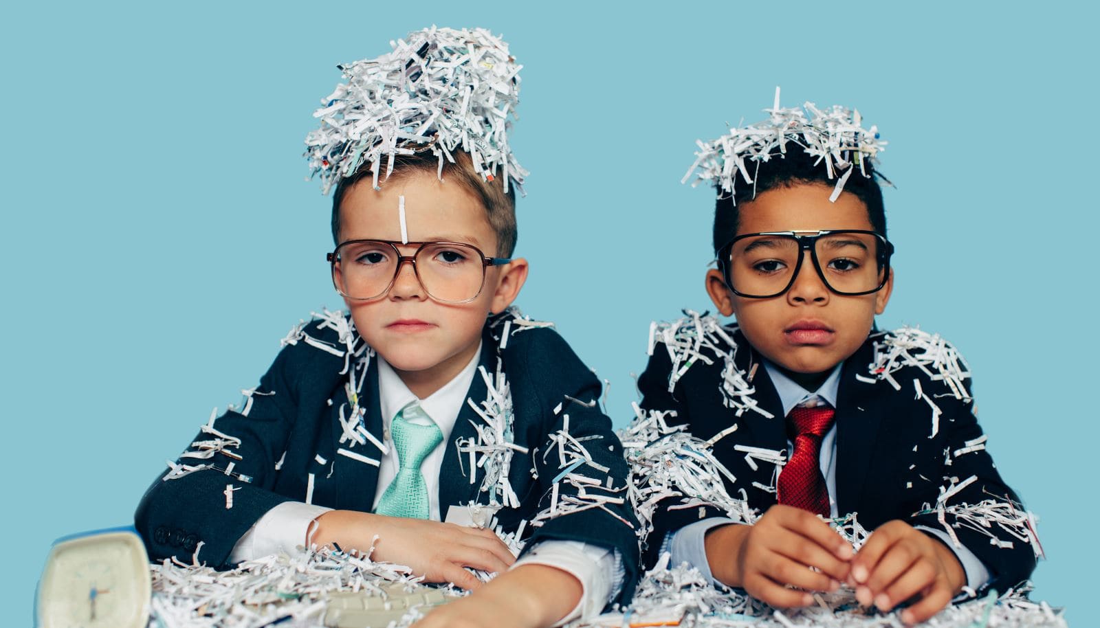 Two suited boys covered with shredded paper, looking furlorn.